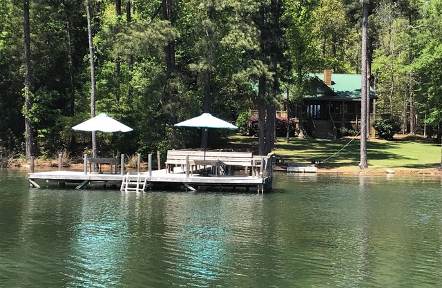 Grand chalet en bois rond: ciel bleu, herbe verte et vie sur le lac